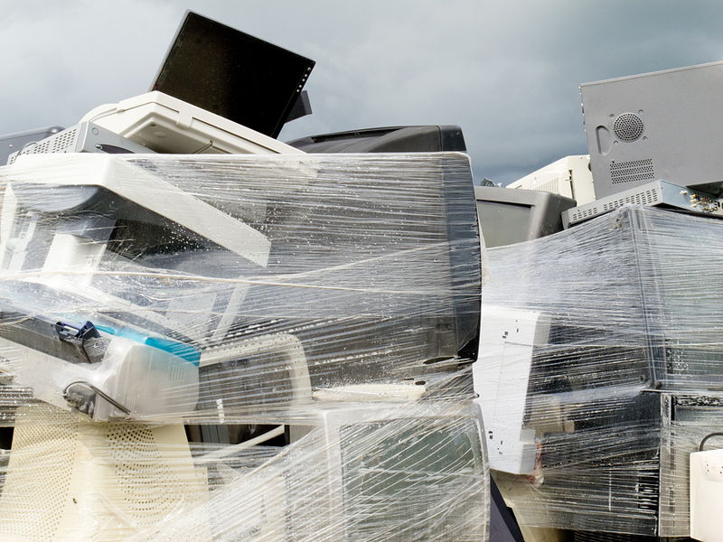 pile of old computer monitors and tech waste wrapped in film